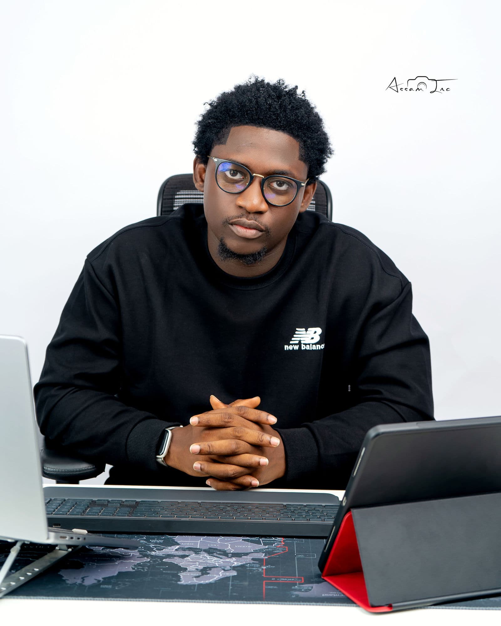 Victor seated at a desk with a laptop and tablet, hands clasped, looking into the camera